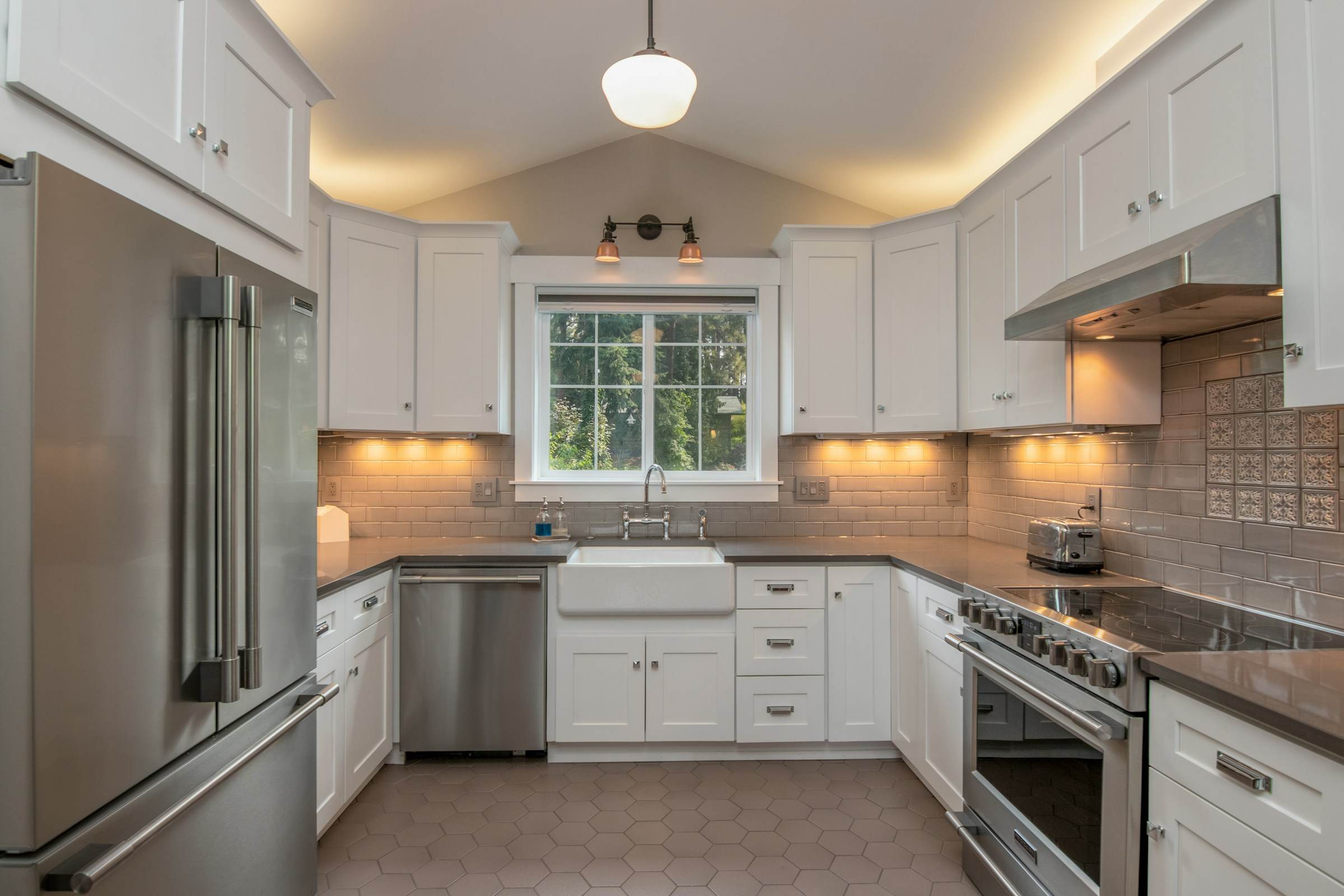 A bright white kitchen with a farmhouse sink, stainless steel appliances and under-cabinet lighting.