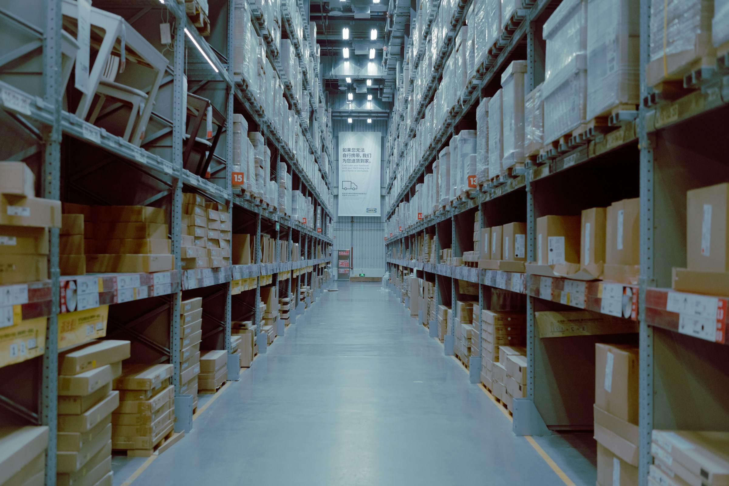 A long warehouse aisle between tall shelves stacked with cardboard boxes.