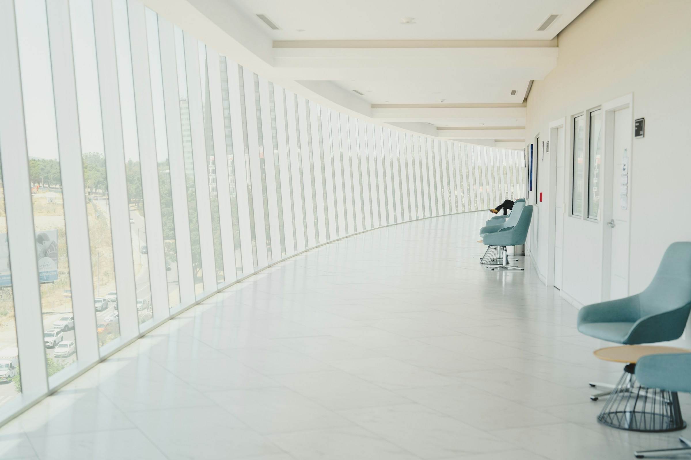 A long, bright hallway with tall windows and a row of waiting-area chairs.