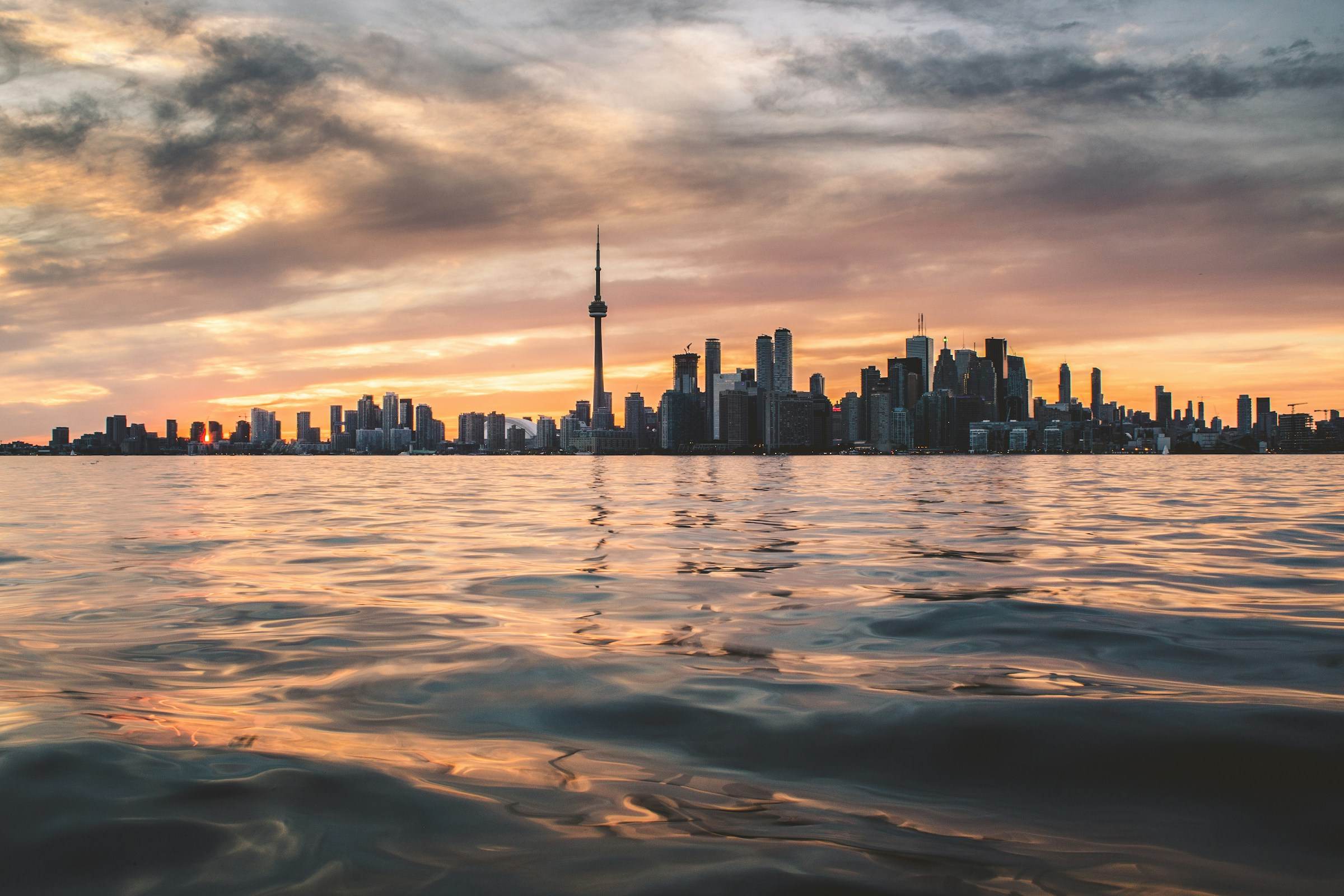 The Toronto skyline and CN Tower across calm lake water at sunset.