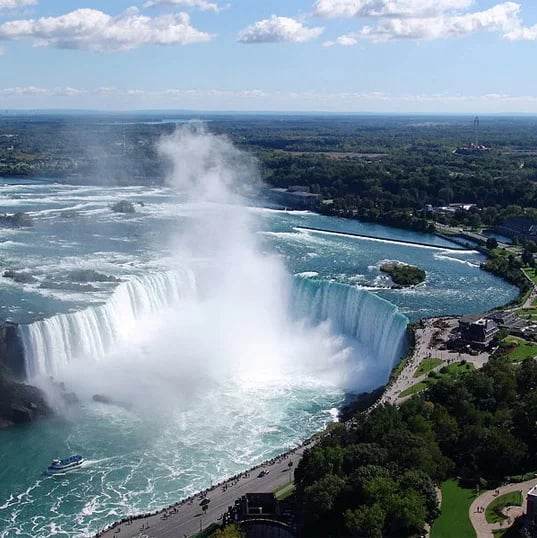 The Horseshoe Falls in Niagara Falls from above, with mist rising and a tour boat below.