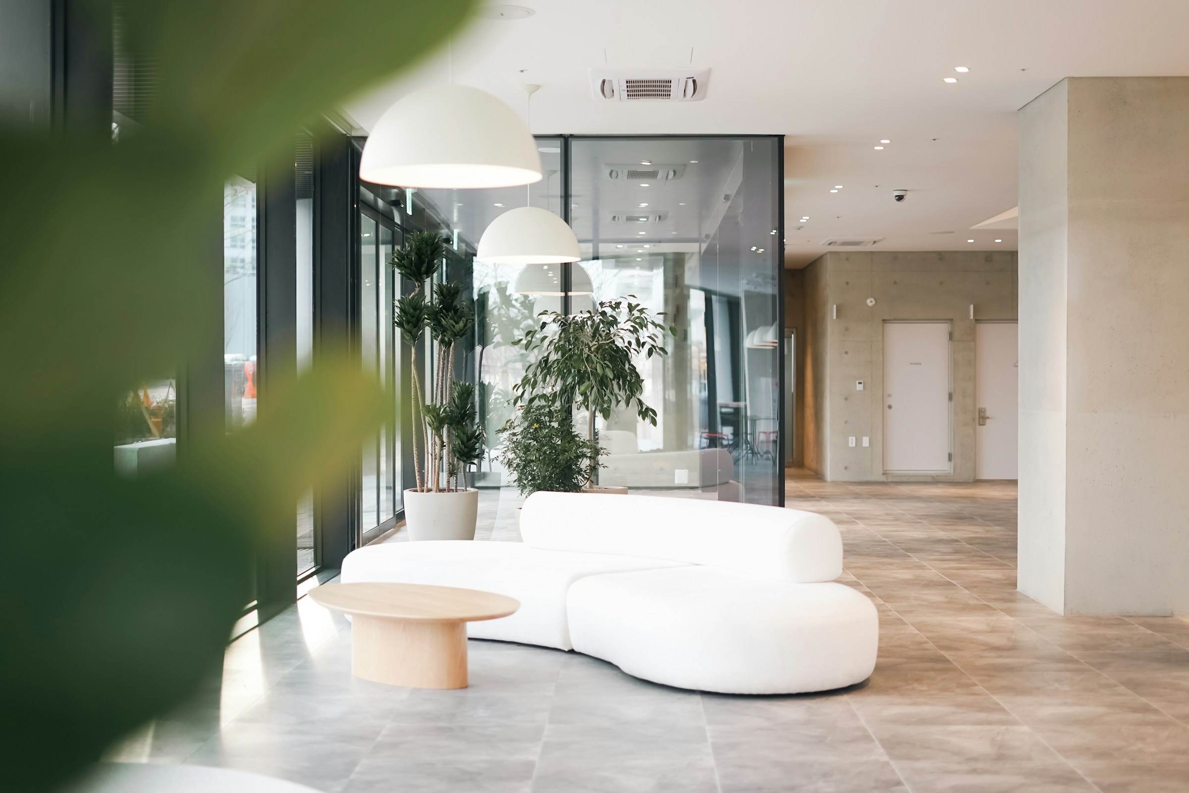 A bright office building lobby with a curved white sofa, pendant lights and plants.