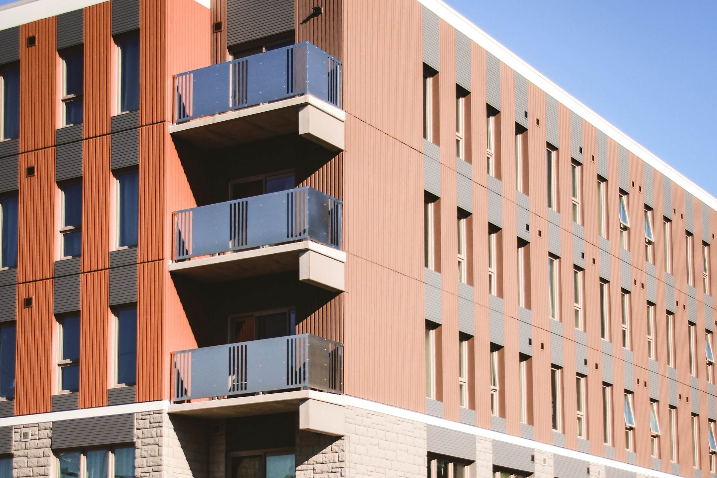 A four-storey apartment building with orange and grey cladding and glass balconies.
