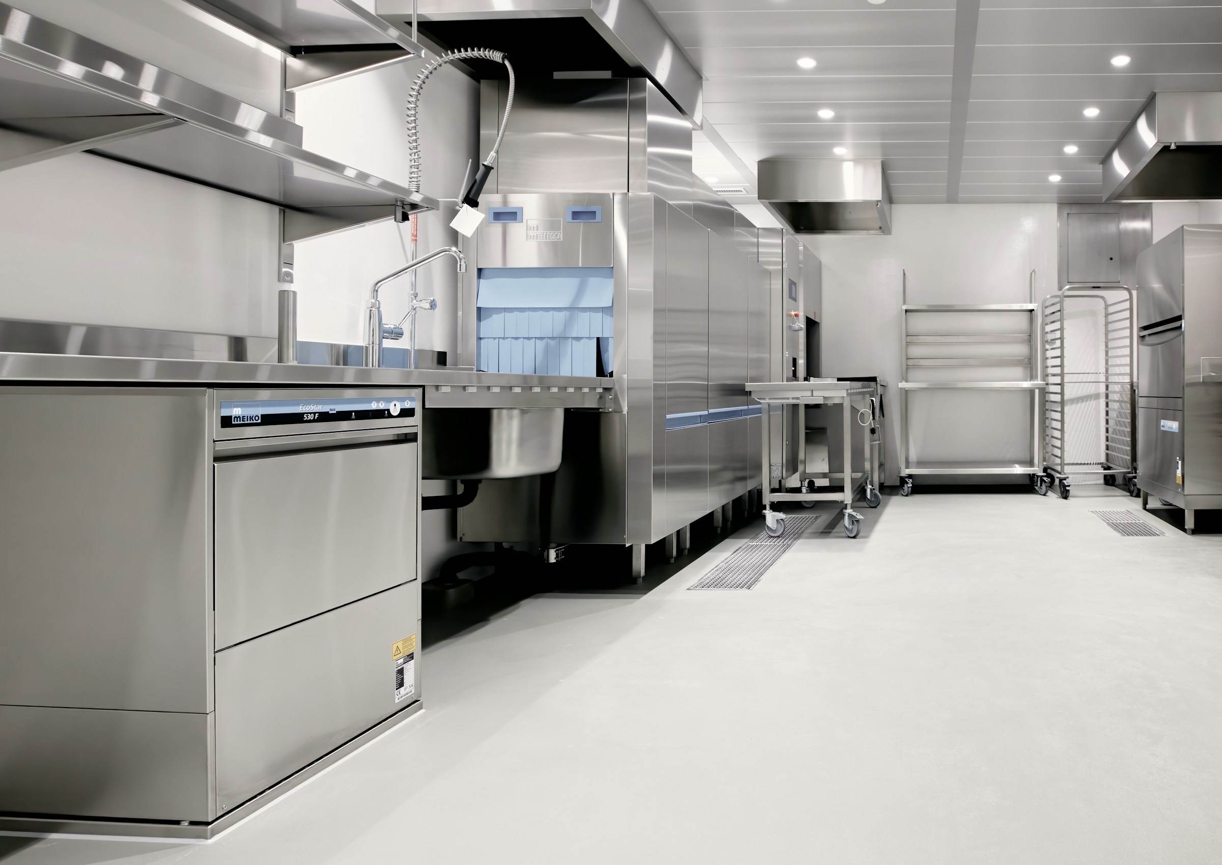 A clean commercial kitchen with stainless steel counters, sinks and dishwashing equipment.