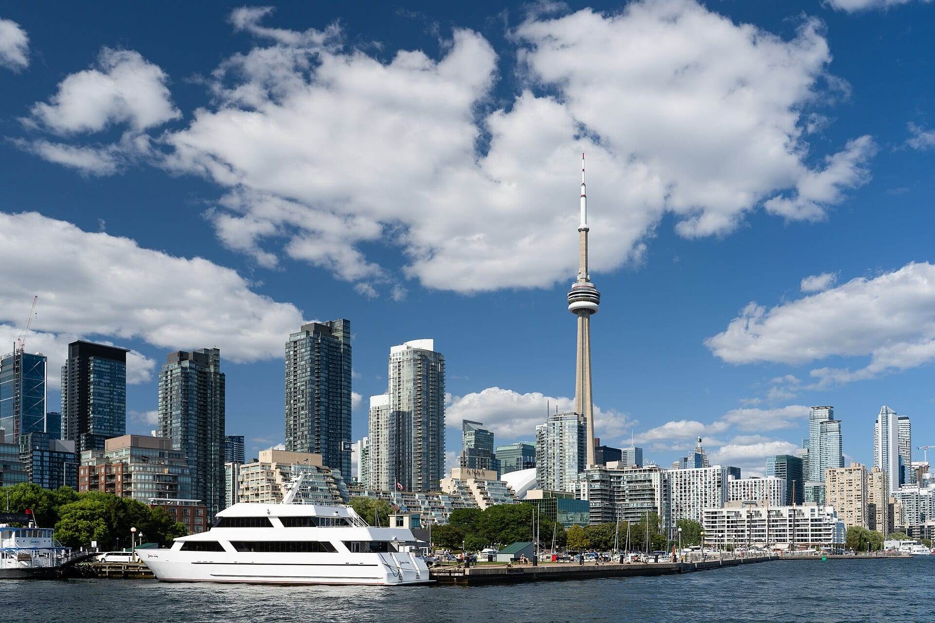 The CN Tower rising above Toronto's waterfront condo towers on a sunny day, seen from across the harbour.