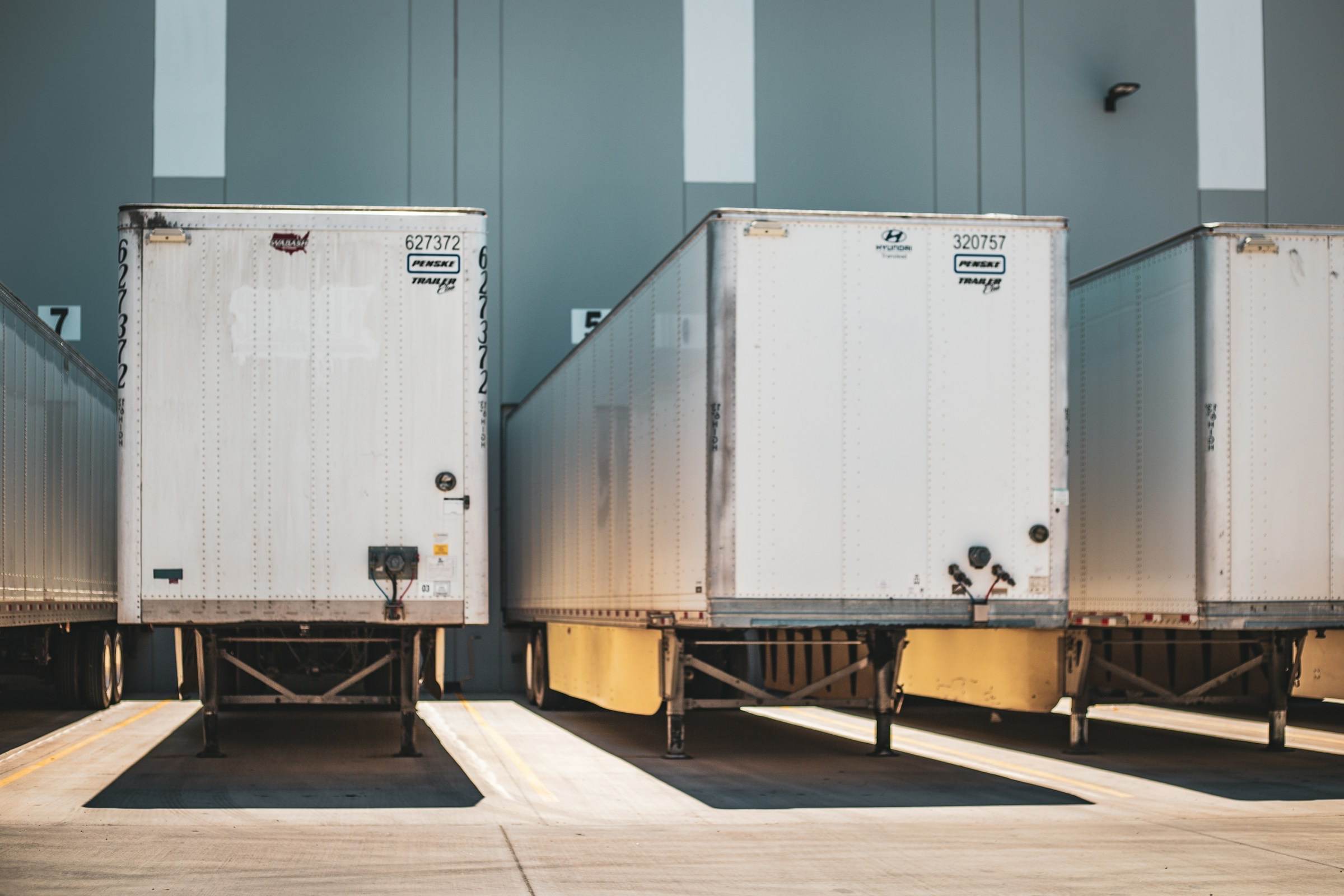 Three white semi-trailers backed up to loading dock doors at a warehouse.